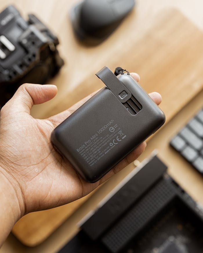 Person holding a compact external hard drive on a desk with tech gadgets around.
